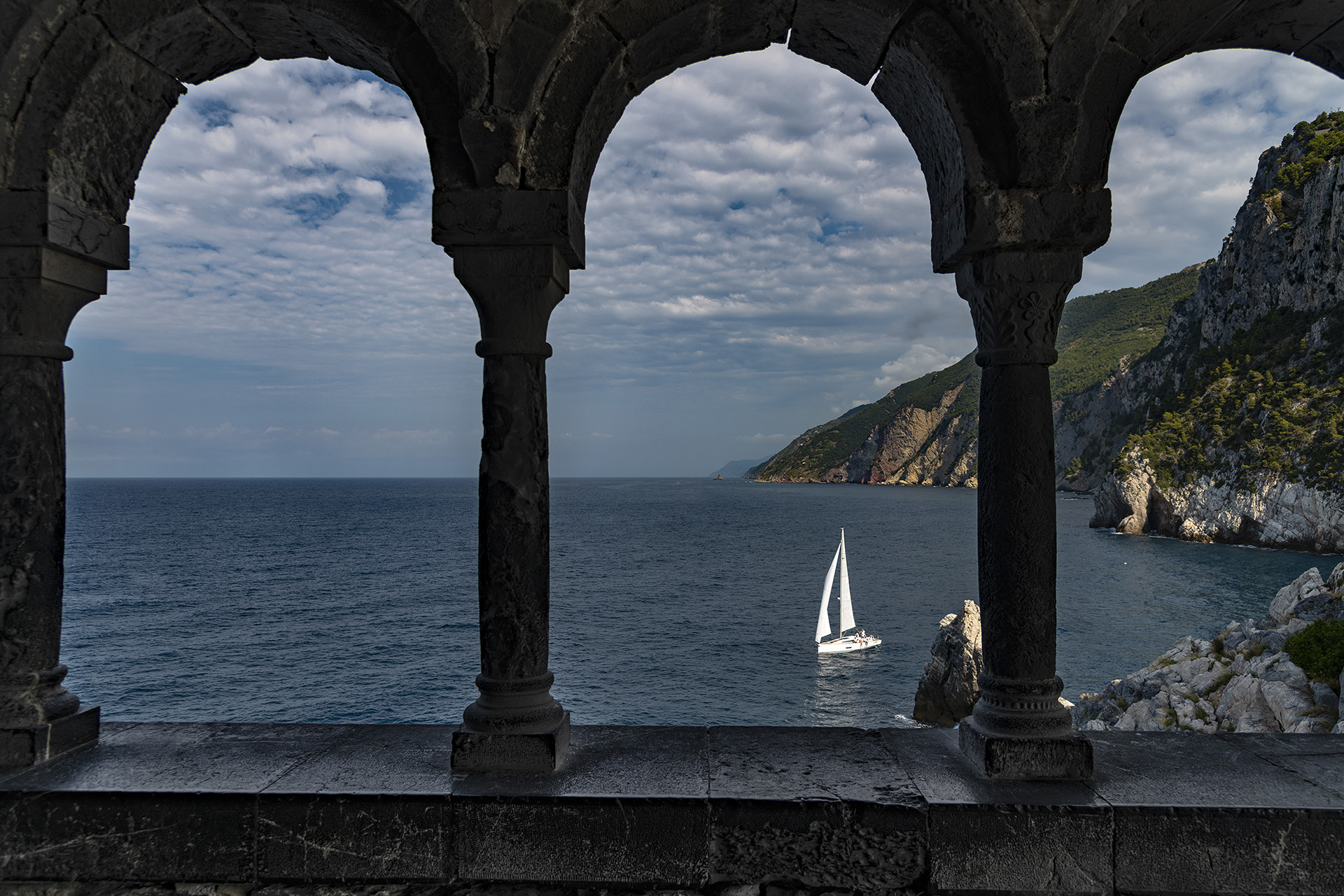Sailing yacht seen through stone arches above the sea