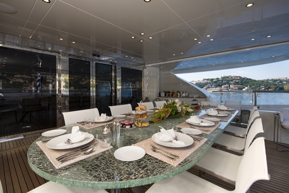 Glass dining table laid on the aft deck, the coast beyond
